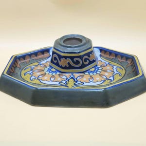 May include: An octagonal ceramic inkwell with a central ink pot and a decorative floral design. The inkwell is primarily dark green with blue and gold accents. The floral design features orange and yellow hues.