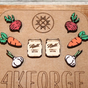 May include: Wooden earrings featuring a red beet, orange carrot, green garlic, and two Ball mason jars. The earrings are displayed on a wooden surface with the text "4KFORGE Cañon City, CO".
