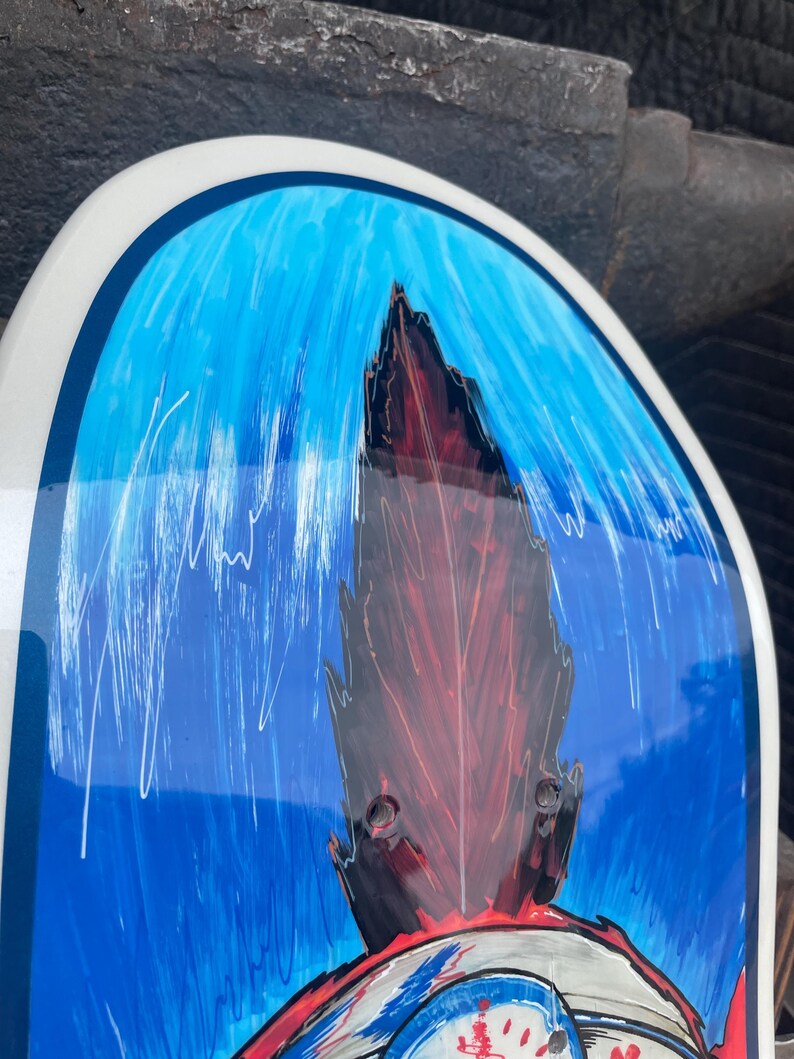May include: A skateboard deck featuring a glossy finish with a vibrant blue background and white vertical brushstroke details. A central dark red and black jagged, flame-like graphic element extends upward, framed by a smooth, rounded white border.
