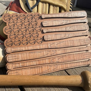 Könnte beinhalten: Amerikanische Flagge aus Holz mit Baseball- und Schlägermotiven. Die Flagge ist aus Holz gefertigt und hat eine natürliche Holzoptik.