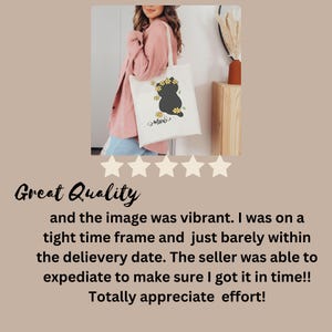 May include: A white tote bag with a black cat silhouette and yellow flowers. The cat is wearing a flower crown and the text "Meow" is printed below the cat. The bag is being held by a person wearing a pink shirt.