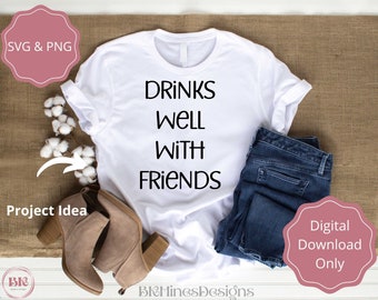 May include: White t-shirt with the text "Drinks Well With Friends" printed in black. The t-shirt is lying on a hessian surface with a pair of brown suede ankle boots and a pair of blue jeans.