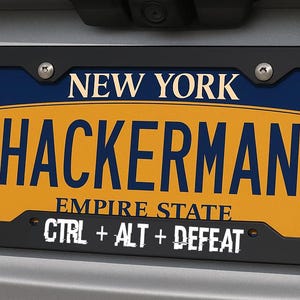 May include: A New York license plate with a black frame. The plate is yellow with the word "HACKERMAN" in large blue letters. Above the word is "NEW YORK" and below is "EMPIRE STATE". The bottom of the plate reads "CTRL + ALT + DEFEAT".