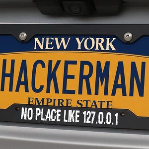 May include: A New York license plate with the word "HACKERMAN" in large blue letters on a yellow background. The plate also says "EMPIRE STATE" and "NO PLACE LIKE 127.0.0.1". The plate is in a black frame.