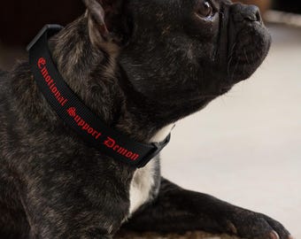 May include: A black dog wearing a black collar with the red text "Emotional Support Demon" on it.