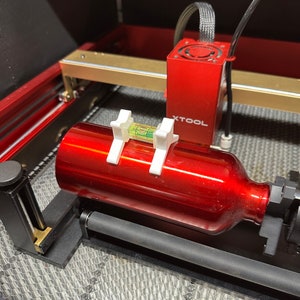 May include: A red metal bottle is secured in a laser cutter with a level attached to the bottle. The laser cutter has a red XTOOL label.