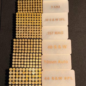 May include: Arrangement of various ammunition types, including .22 LR, 9mm, .380 Auto, and .45 ACP. Each type is displayed with its corresponding label, providing clear identification. The cartridges are arranged in neat rows.