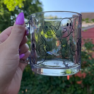 May include: A clear glass mug with a black outline of ghosts and bats. The mug has a glittery iridescent finish.