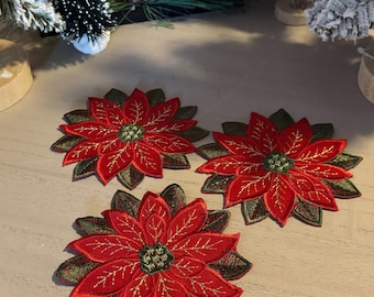 Peut inclure: Trois écussons brodés en forme de fleur de poinsettia. Chaque écusson présente des pétales rouges vifs avec des accents dorés et des feuilles vertes. Le centre de chaque fleur est un motif vert détaillé. Idéal pour les travaux manuels de Noël.