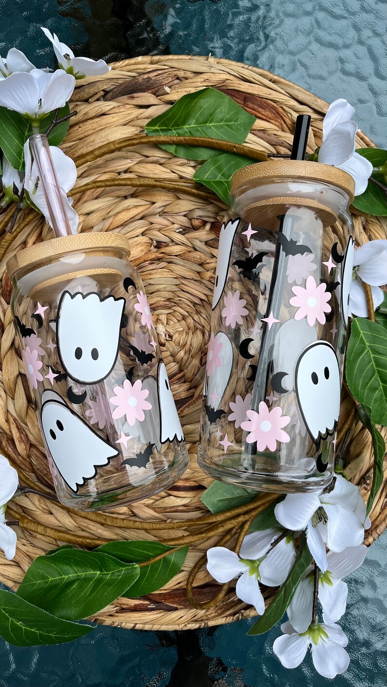 May include: Two clear glass tumblers with bamboo lids and straws. The tumblers feature a spooky Halloween design with pink flowers, bats, and ghosts.
