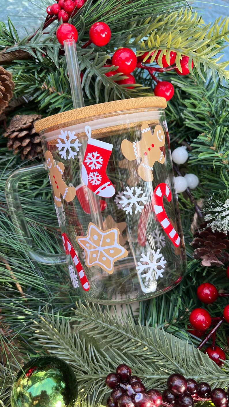 May include: A clear glass mug with a bamboo lid and a straw. The mug has a Christmas theme with gingerbread men, snowflakes, candy canes, and stockings.