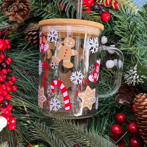 May include: A clear glass mug with a bamboo lid and a straw. The mug has a Christmas theme with gingerbread men, candy canes, snowflakes, and stars.