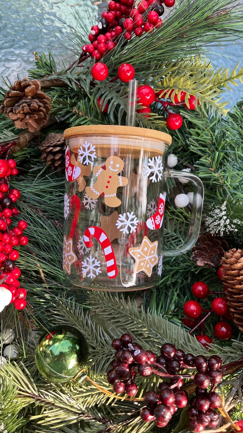 May include: A clear glass mug with a bamboo lid and a straw. The mug has a Christmas theme with gingerbread men, candy canes, snowflakes, and stars.