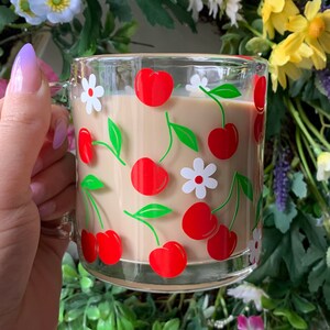 May include: A glass mug with a cherry and flower design. The mug is filled with a light brown beverage.
