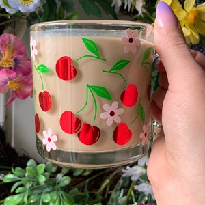 May include: A glass mug with a cherry and flower design. The mug is filled with a light brown beverage.