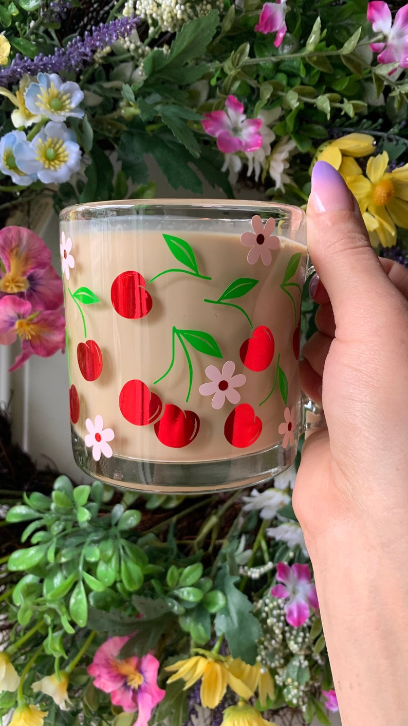May include: A glass mug with a cherry and flower design. The mug is filled with a light brown beverage.