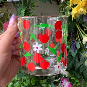 May include: A clear glass mug with a red and green cherry and white flower design.