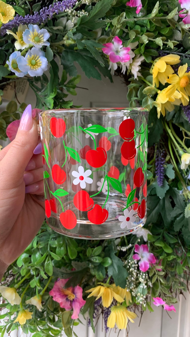 May include: A clear glass mug with a red and green cherry and white flower design.