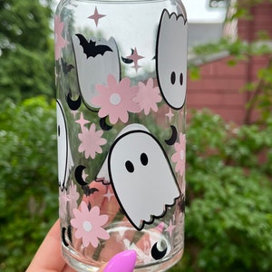 May include: A clear glass can with a pink and white ghost, flower, and crescent moon design. The can is decorated with a black bat and stars.