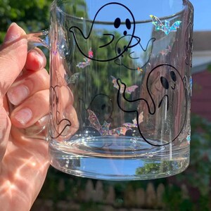 May include: A clear glass mug with a black outline of ghosts and bats. The ghosts have two black dots for eyes. The bats have iridescent glitter.