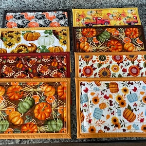May include: Eight different autumn-themed placemats with various designs featuring pumpkins, sunflowers, and fall foliage. The placemats are all rectangular and have a brown, orange, and yellow color scheme.