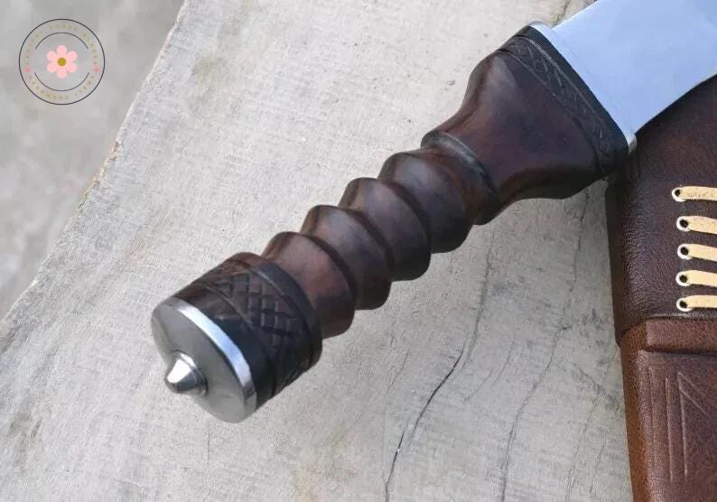 Pu&ograve; includere: Primo piano di un coltello fatto a mano con un manico in legno marrone scuro a spirale e un'estremit&agrave; in metallo argentato. La lama &egrave; parzialmente visibile, cos&igrave; come un fodero in pelle marrone con cuciture decorative.