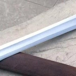 Pu&ograve; includere: Una spada color argento con una lama dritta e un fodero in pelle marrone. La spada ha un'impugnatura rettangolare e una punta affilata. Il fodero presenta cuciture decorative e piccoli anelli. La spada &egrave; su una superficie di legno.