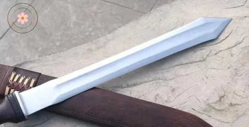 Pu&ograve; includere: Una spada color argento con una lama dritta e un fodero in pelle marrone. La spada ha un'impugnatura rettangolare e una punta affilata. Il fodero presenta cuciture decorative e piccoli anelli. La spada &egrave; su una superficie di legno.