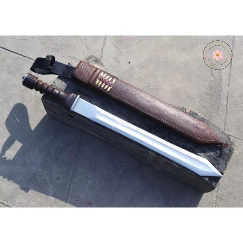 Pu&ograve; includere: Una spada romana gladius con manico in legno e lama argentata brillante. La spada &egrave; appoggiata su un blocco di legno accanto al suo fodero in pelle marrone, con cuciture decorative e un design intagliato.
