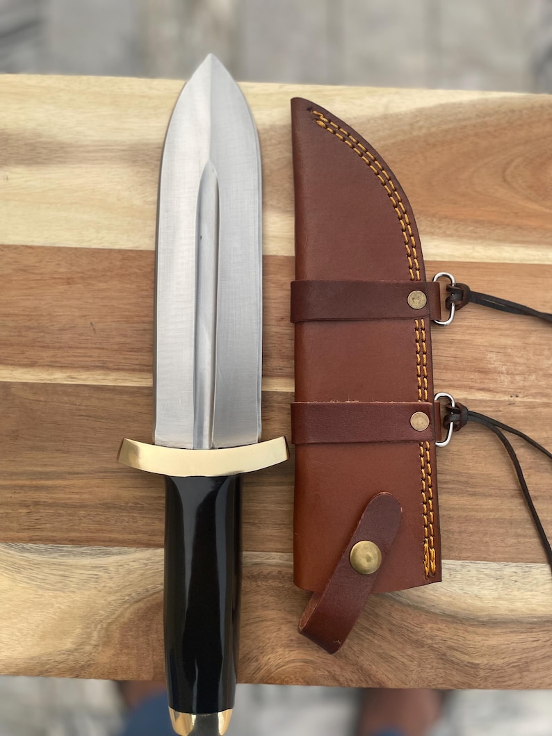 Pu&ograve; includere: Un pugnale d'argento con manico nero e guardia in ottone. Il pugnale &egrave; in un fodero di cuoio marrone con un bottone in ottone e cuciture.