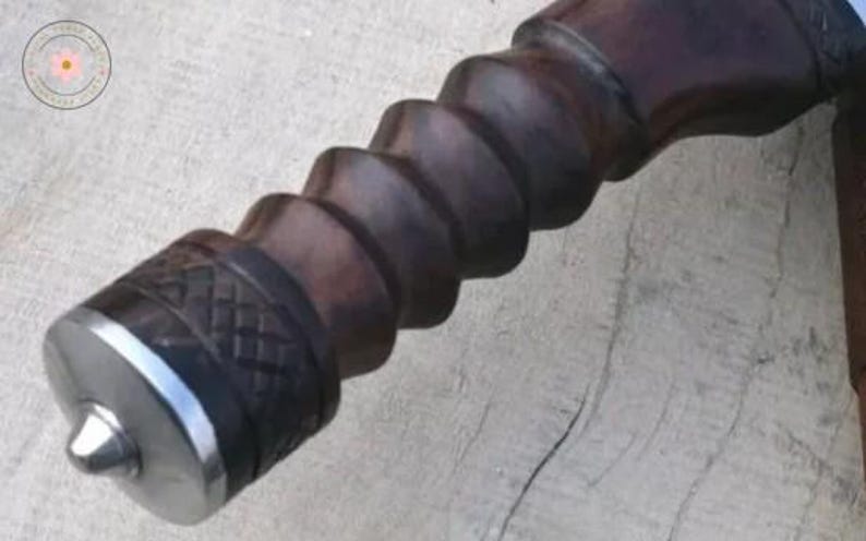 Pu&ograve; includere: Primo piano di un manico in legno marrone scuro con un design a spirale. Il manico ha un'estremit&agrave; in metallo argentato con una punta e una fascia decorativa. La venatura del legno &egrave; visibile e il manico sembra far parte di uno strumento.