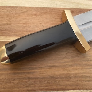 Pu&ograve; includere: Un coltello nero e dorato con manico in legno. La lama &egrave; in metallo e ha una punta affilata. Il manico &egrave; in legno e ha un tappo in metallo dorato.