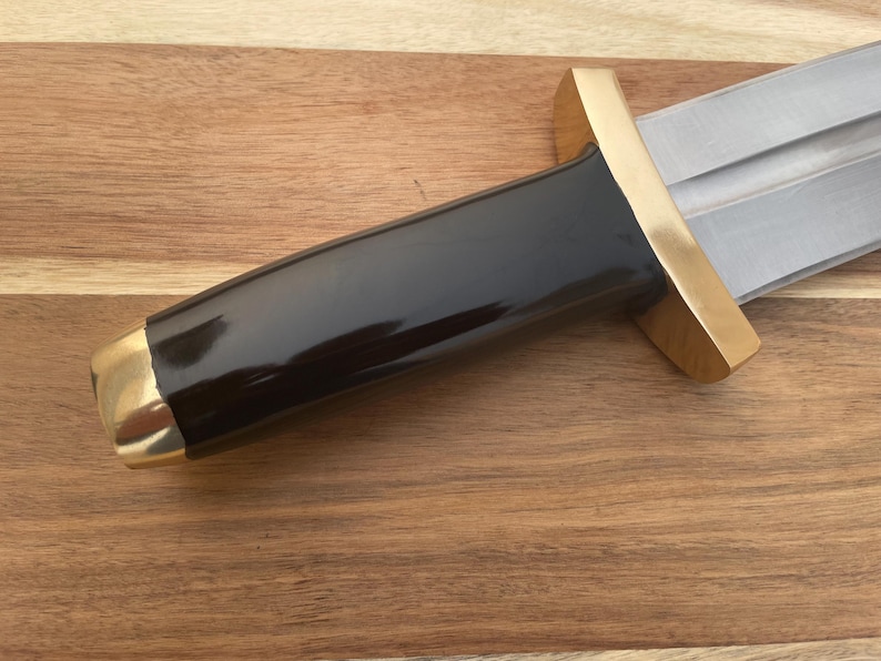 Pu&ograve; includere: Un coltello nero e dorato con manico in legno. La lama &egrave; in metallo e ha una punta affilata. Il manico &egrave; in legno e ha un tappo in metallo dorato.