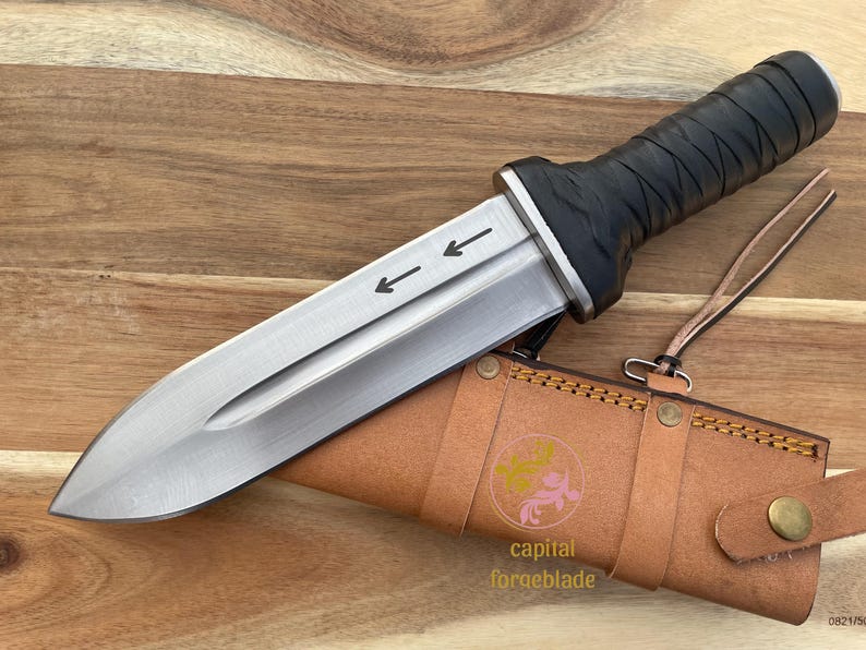 Pu&ograve; includere: Un coltello avvolto in pelle nera con una lama argentata e un fodero in pelle marrone. La lama ha due frecce che puntano verso il manico, incise sulla lama.