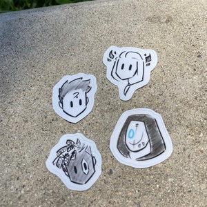 May include: Four black and white cartoon character stickers on a gray concrete surface. The stickers are round and feature different characters with simple facial features.