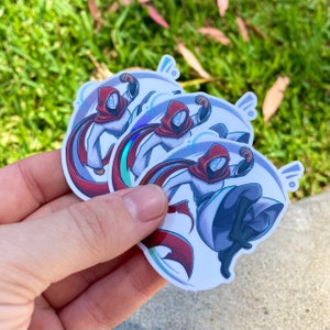 May include: Three holographic stickers featuring a white-clad figure with a red hood and cape, set against a swirling blue background.