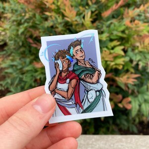 May include: A sticker featuring a drawing of two people with blue and white flames around their heads. The person on the left is holding a white mask to their face. The person on the right is wearing a green and white toga. The sticker has a purple background and the text "Spot" in the upper right corner.
