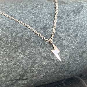 May include: A silver chain necklace with a small lightning bolt pendant.