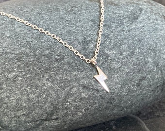 May include: A silver chain necklace with a small lightning bolt pendant.