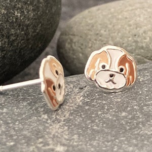 Op de afbeelding: Een paar zilveren oorbelletjes met een cartoon hondenkop van bruin en wit emaille. De hond heeft zwarte ogen en een bruine neus.