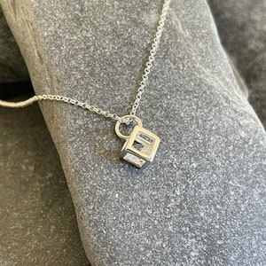 May include: A silver chain necklace with a small, cubic pendant. The pendant is made of silver and has a geometric design.