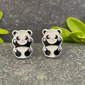 May include: A pair of silver panda bear stud earrings. The panda bears are black and white with a white face and black eyes.