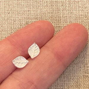 May include: A pair of silver leaf earrings. The leaves are textured and have a delicate design.