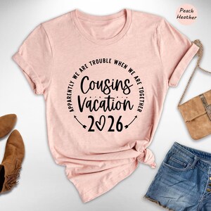a pink t-shirt with a humorous text, a pair of jeans, a pair of brown boots, and a beige handbag, all arranged on a white background.