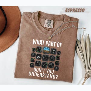 May include: An espresso-coloured t-shirt featuring a graphic of various aeroplane cockpit instrument gauges arranged in a grid. The text "WHAT PART OF" appears above the gauges and "DON'T YOU UNDERSTAND?" appears below in white lettering.