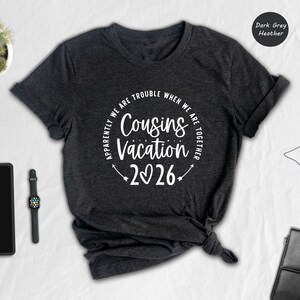 a casual outfit laid out on a white surface, including a black t-shirt with a humorous text, a tablet, a watch, a potted plant, and a black bag.