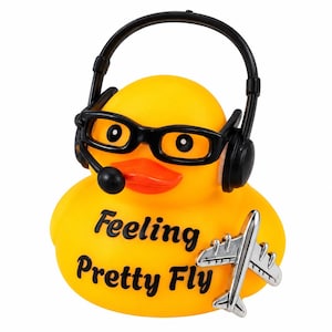 May include: A bright yellow rubber duck wearing black glasses and a black headset with a microphone. The duck features the black text "Feeling Pretty Fly" on its chest and holds a small silver-colored airplane figurine on its right side.
