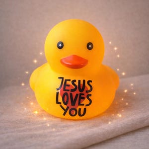 May include: A yellow rubber duck with black eyes and an orange beak. The text "JESUS LOVES YOU" is printed in black on the duck's chest. The duck is a religious-themed item.