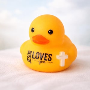 May include: A yellow rubber duck with black eyes and an orange beak. The text "JESUS LOVES you" is printed on the duck's chest, along with a white cross. The duck is a religious-themed item.