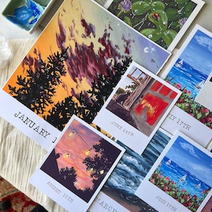 May include: A collection of eight painted cards with different scenes and dates. The dates are written in a handwritten font. The cards are arranged in a random order on a table. The cards are all different sizes and shapes.